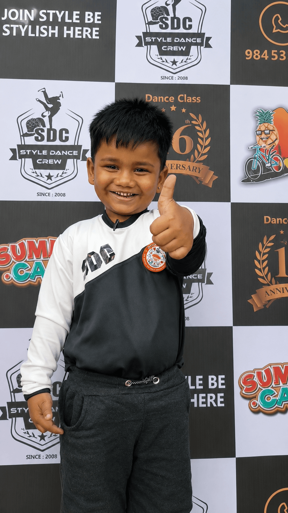 A young student in Style Dance Crew uniform holding a medal in front of the studio backdrop.