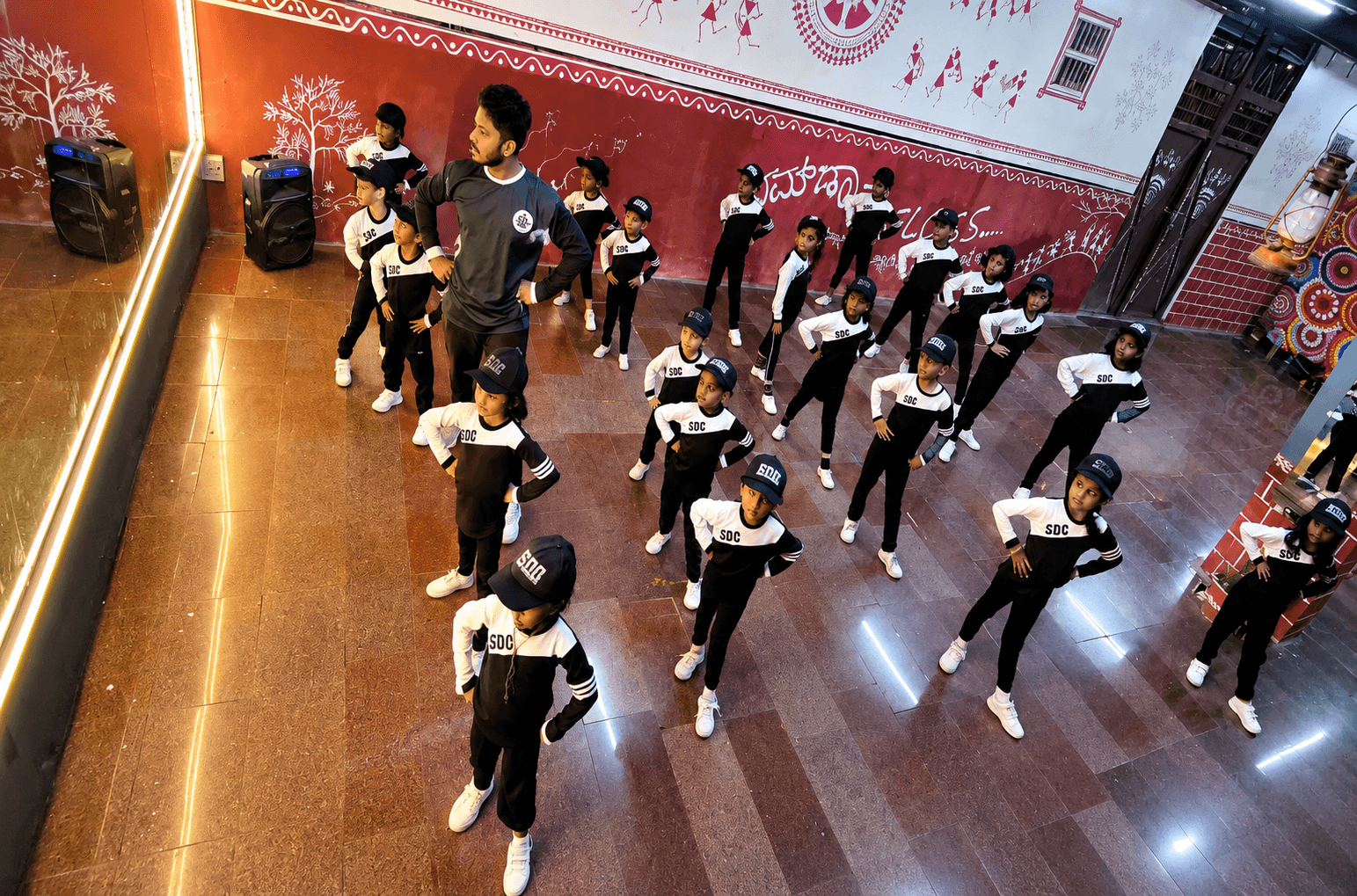 An SDC instructor leading a junior batch in formation beside the mirror wall
