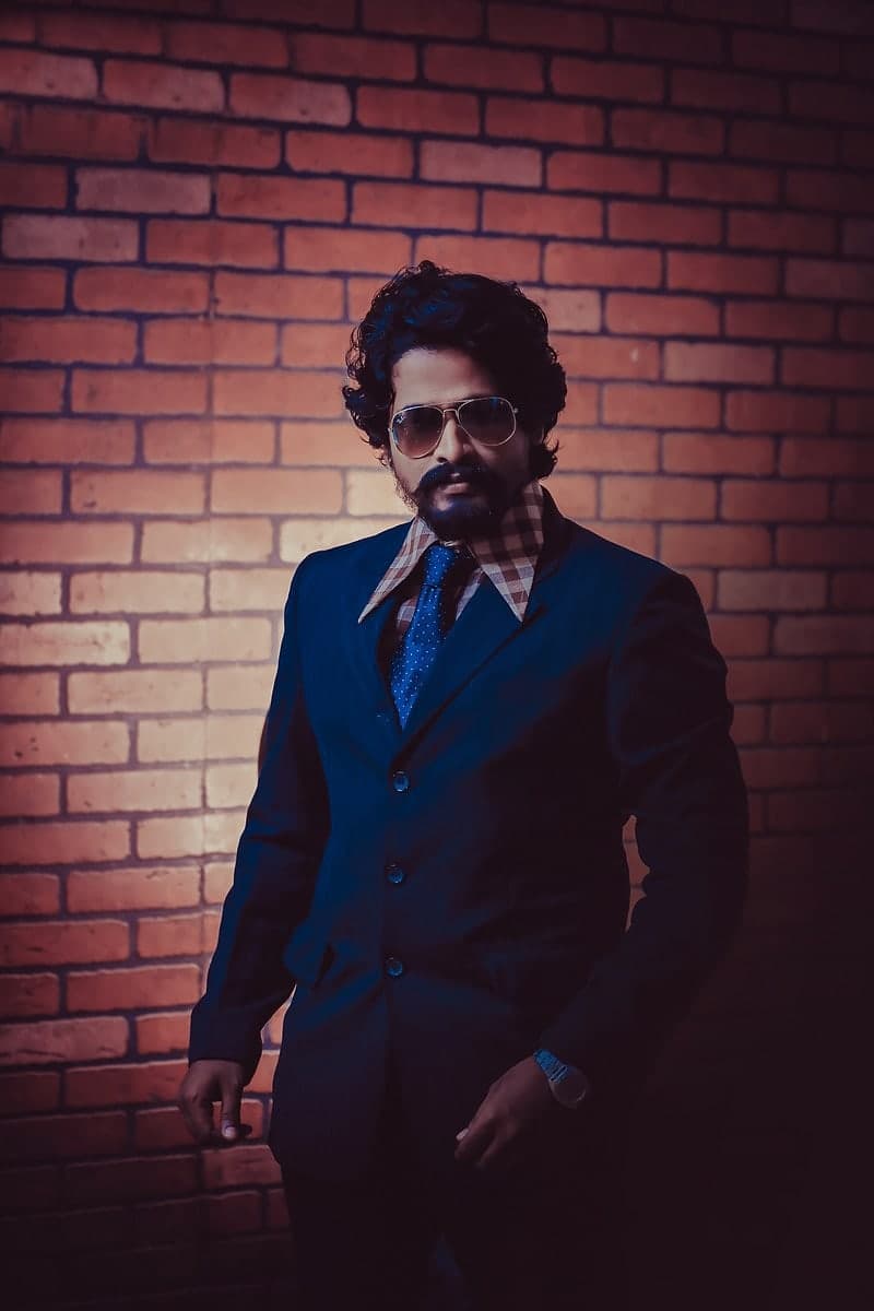 Shashikumar N. photographed against a brick wall — the portrait reproduced on his 2025 Natya Sarvabhouma citation.